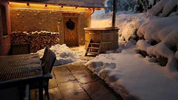 A snow-covered outdoor area with a wooden structure, a hot tub, and a stack of firewood. - Vacation apartment Rosenheim (Rosenheim)