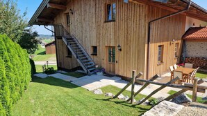 A wooden cabin with a staircase leading to the entrance, a patio with a table and chairs, and a view of the surrounding landscape. - Vacation apartment Rosenheim (Rosenheim)