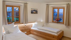 A room with two beds, wooden flooring, and large windows with curtains. - Vacation apartment Rosenheim (Rosenheim)