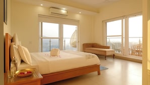 A modern bedroom with a large bed, a sitting area, and large windows offering a city view. - Golden Healing Journeys Homestay (Rishikesh)