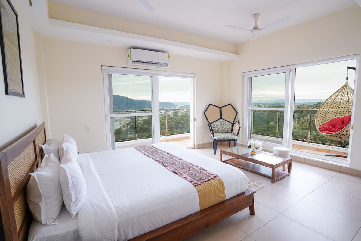 A bedroom with a large bed, a hanging chair, and a balcony with a view.