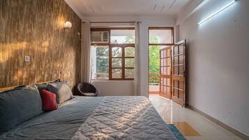 A bedroom with a bed, a wooden wall, a window, and a door leading outside.