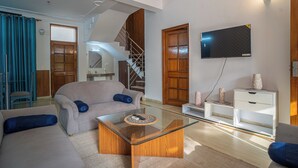 A modern living room with a glass coffee table, a sofa, a TV mounted on the wall, and a staircase leading to another level. - Golden Healing Journeys Homestay (Rishikesh)