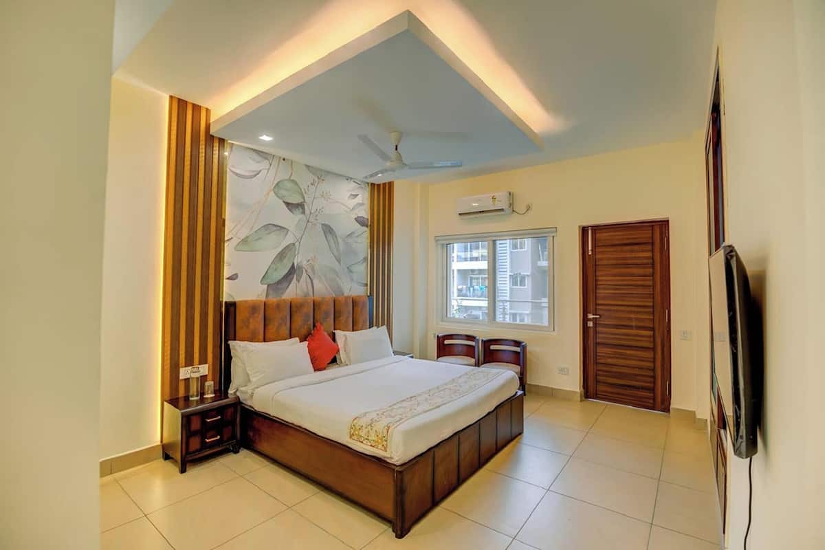 A bedroom with a large bed, a ceiling fan, an air conditioning unit, a TV, and a window with blinds.
