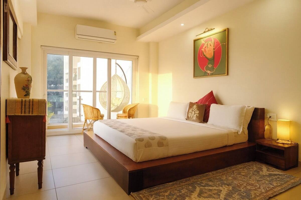A spacious bedroom with a large bed, a sitting area with chairs, a large window, and a wall-mounted artwork.