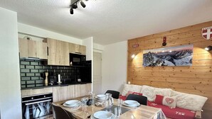A modern kitchen with a dining area, wooden walls, and a mountain painting.