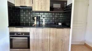 A compact kitchen with wooden cabinets, a black countertop, a built-in microwave, and a dishwasher.