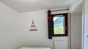 A bedroom with a bed, a window with curtains, a radiator, and a wall decoration.