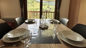 A dining table set with plates, glasses, and a pitcher, with a scenic view of a green landscape through a window.