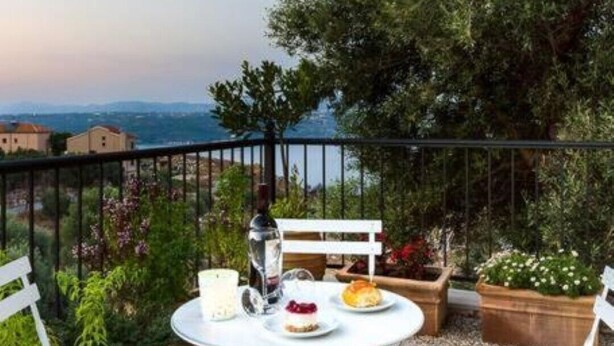 A terrace with a table set for two, surrounded by a railing, overlooking a scenic view. - Villa Alysso, fully equipped, modern with shared pool & sea and mountain view (Aptera)