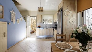 A modern kitchen with wooden cabinets, a stone wall, and a dining area with a table and chairs. - Villa Alysso, fully equipped, modern with shared pool & sea and mountain view (Aptera)