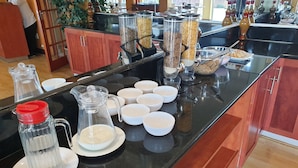 Un buffet de petit-déjeuner comprenant des récipients de céréales, des bols et un pichet de lait.
