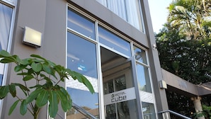 Une entrée d'hôtel moderne avec une façade en verre, une enseigne indiquant « HÔTEL CUBE », et un escalier menant à l'entrée.