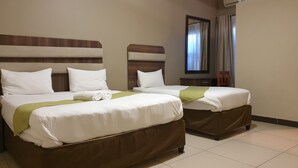 Une chambre d’hôtel avec deux lits, chacun étant équipé de draps blancs et d’une tête de lit marron. Un plaid vert est posé sur l’un des lits et un miroir est accroché au-dessus du lit.