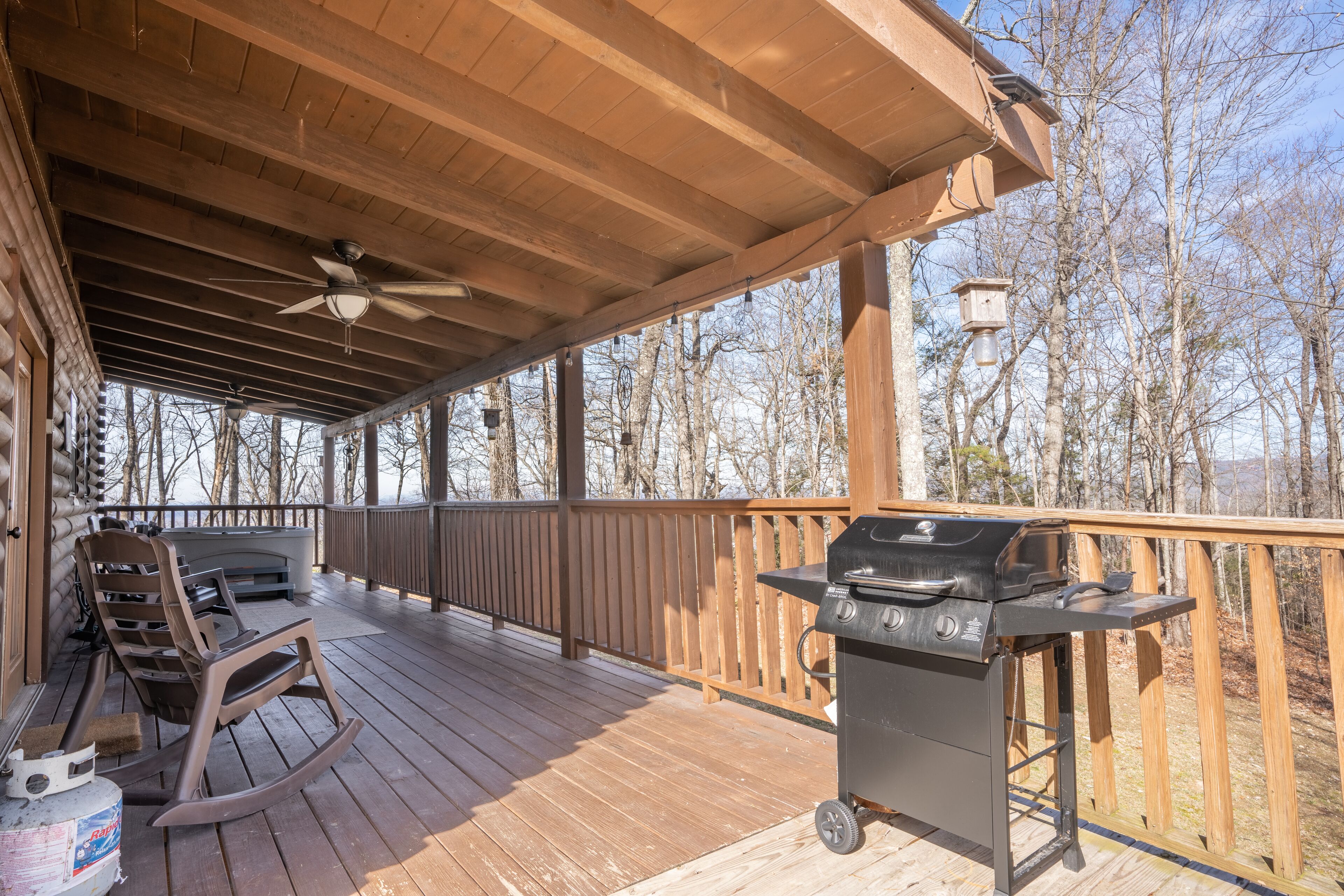 A covered wooden deck with a grill, chairs, and a ceiling fan.