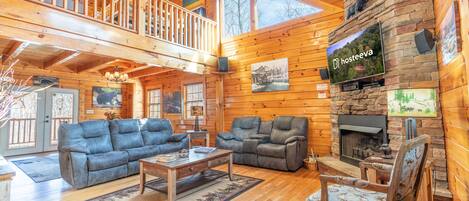 A spacious wooden cabin with a living room featuring two sofas, a coffee table, and a fireplace.