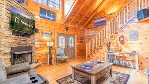 A cozy log cabin interior with a stone fireplace, a comfortable sofa, a wooden coffee table, and a staircase leading to the upper level. - Comfort Cabin Bearway To Heaven - w Private Hot Tub (Pigeon Forge)