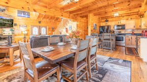 A wooden cabin interior with a dining area, kitchen, and a staircase leading to the upper level. - Comfort Cabin Bearway To Heaven - w Private Hot Tub (Pigeon Forge)