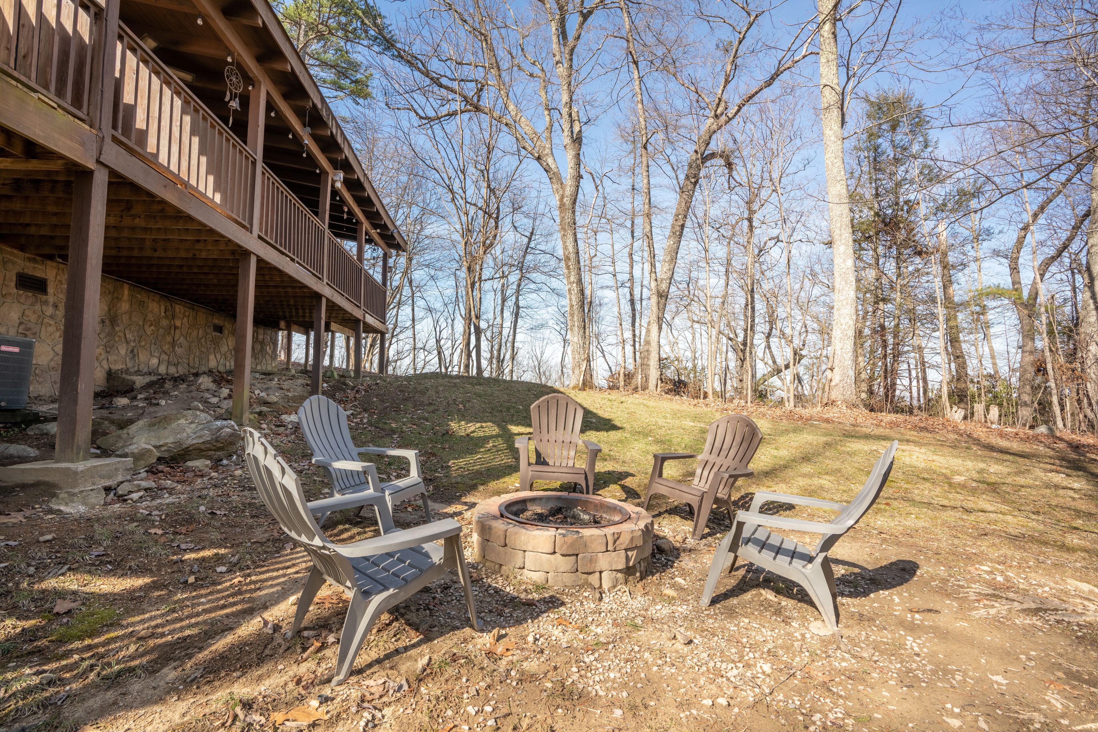 A wooden deck with Adirondack chairs arranged around a stone fire pit.
