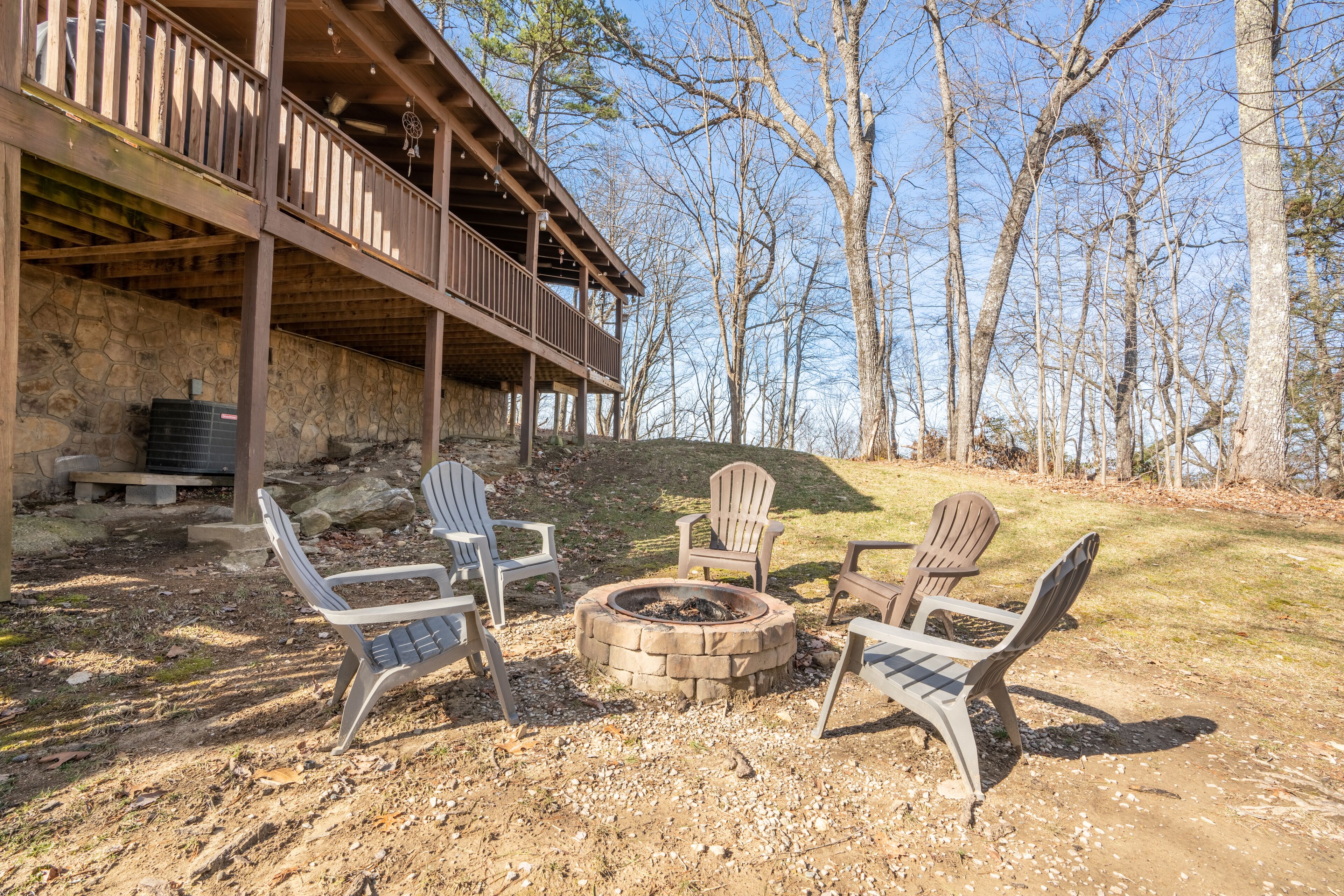A rustic cabin with a stone fireplace, outdoor seating, and a wooden deck overlooking a forested area.