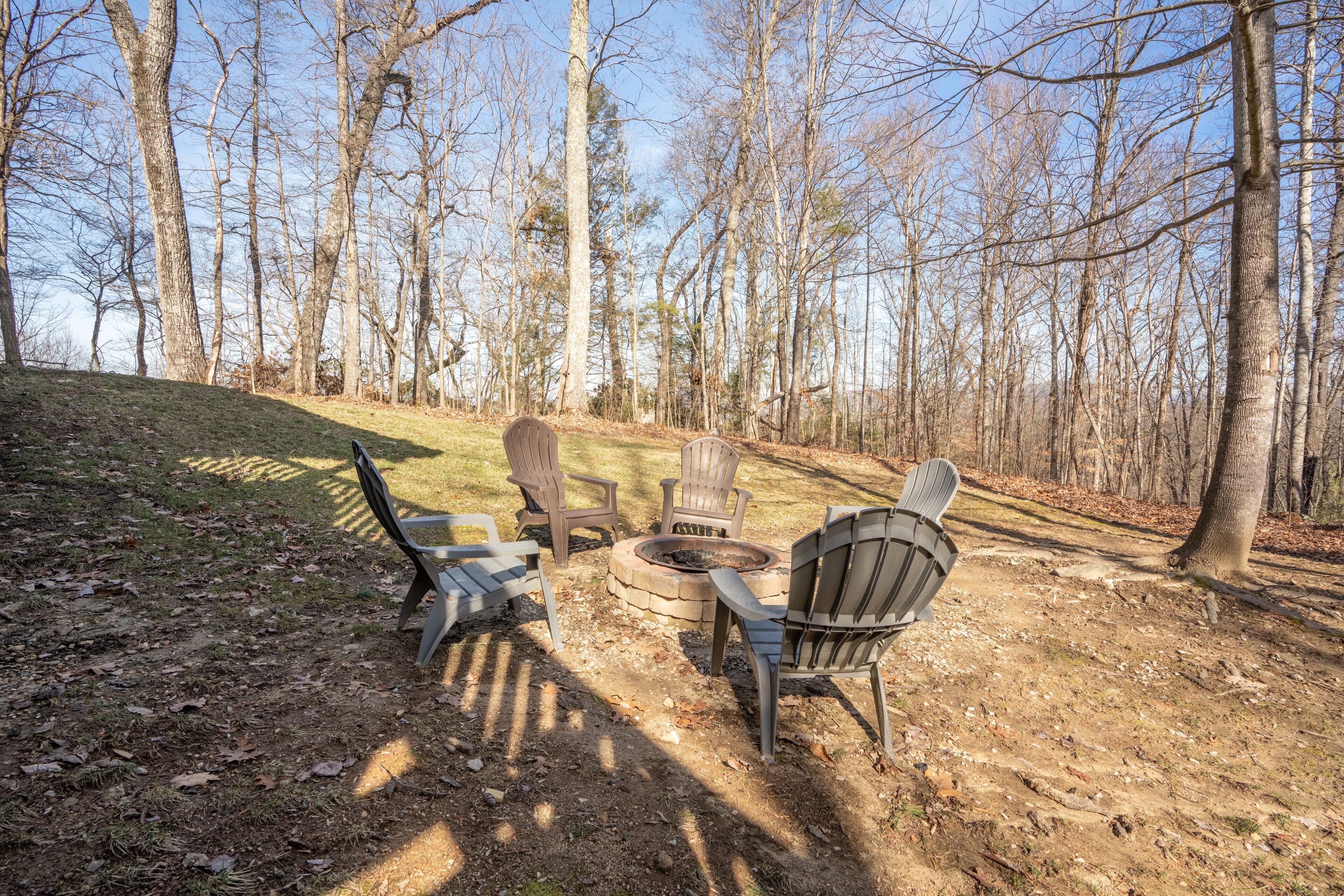 Un espace aménagé avec un foyer et des fauteuils Adirondack, le tout situé dans un cadre boisé.