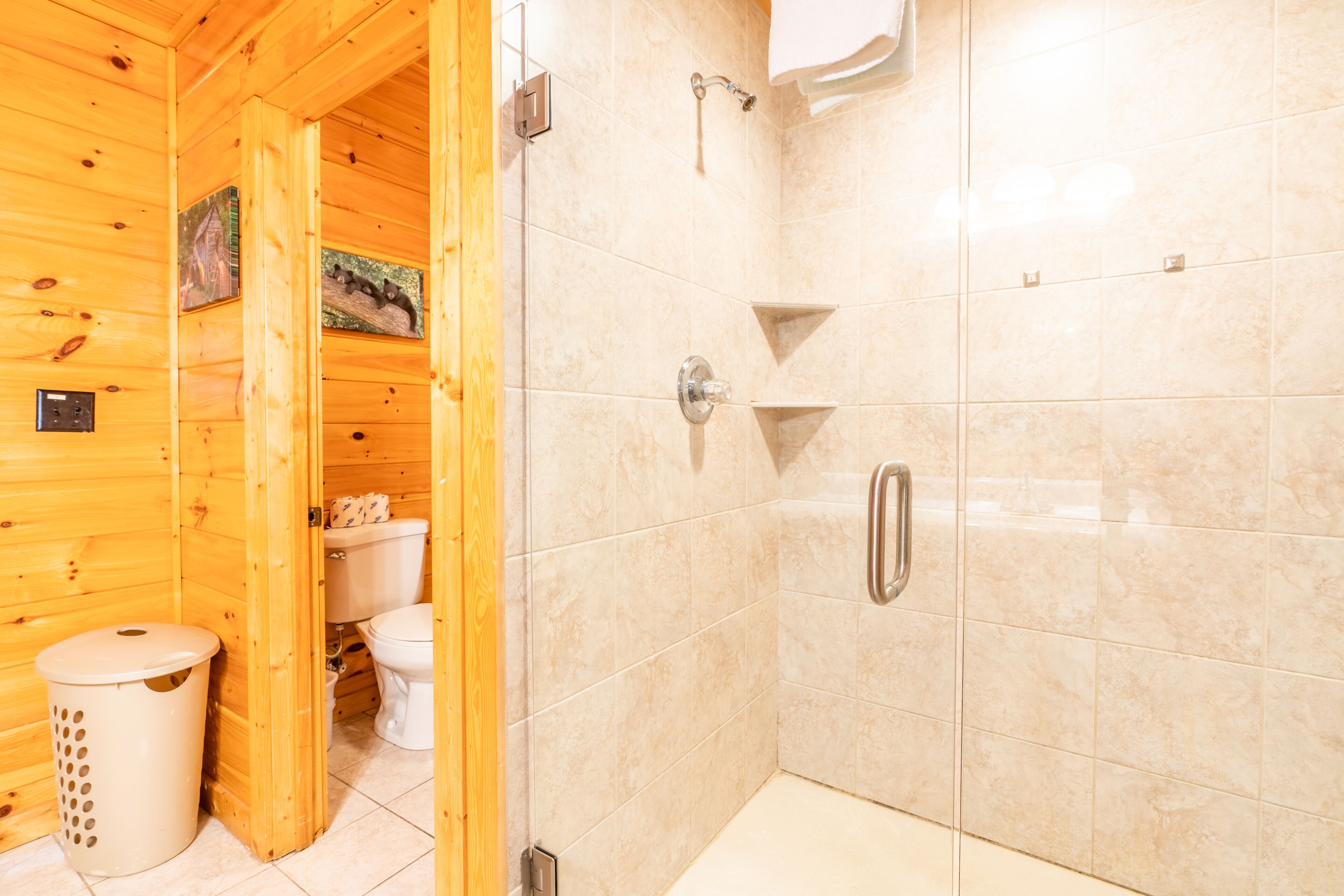 A wooden cabin bathroom with a shower, toilet, and a trash can.