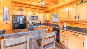 A wooden cabin-style kitchen with a central island, wooden cabinets, and a stainless steel refrigerator. - Comfort Cabin Bearway To Heaven - w Private Hot Tub (Pigeon Forge)