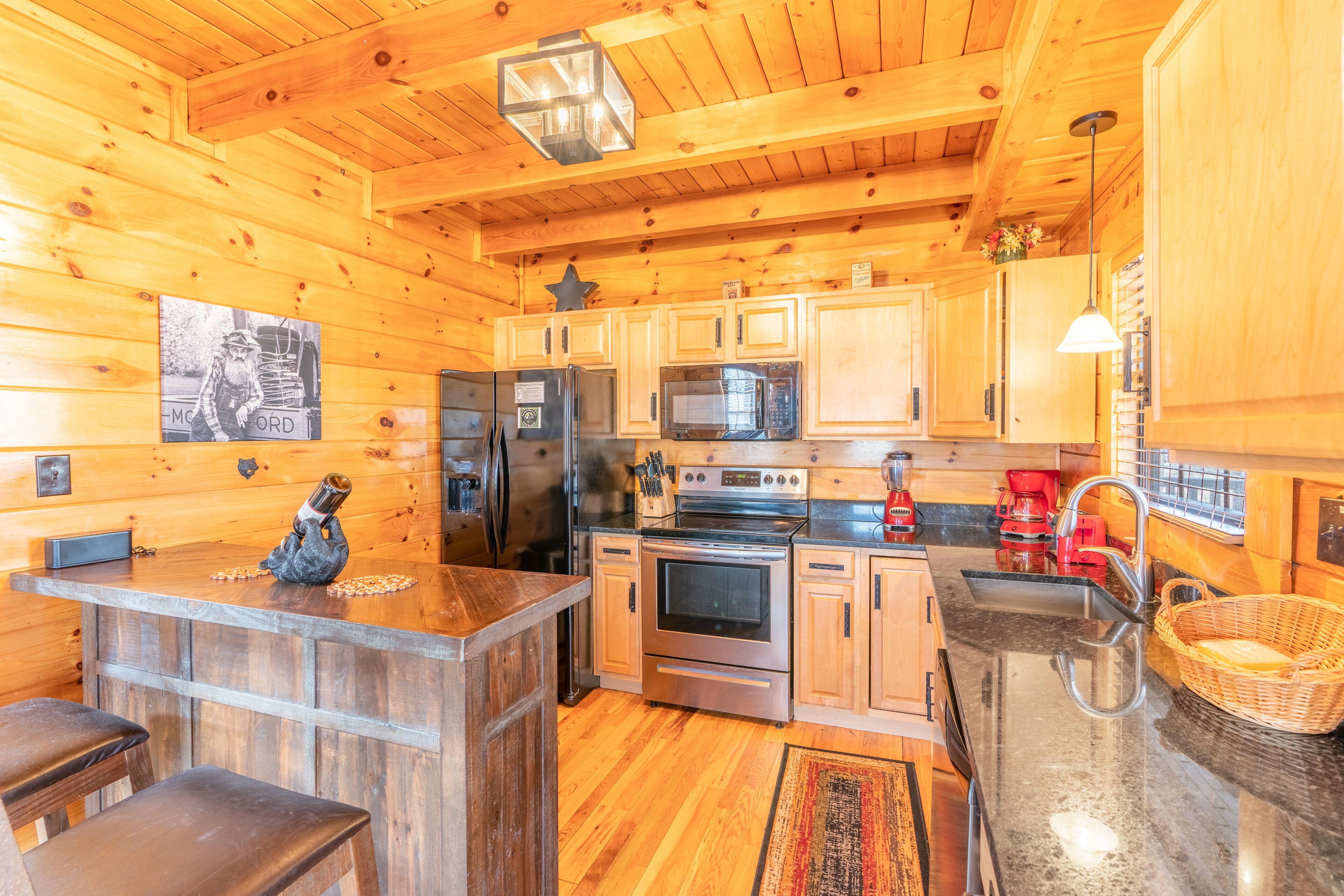 A wooden cabin interior with a kitchen featuring a refrigerator, stove, microwave, and wooden cabinets.