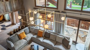 Ein großzügiger Wohnbereich mit einer großen Couch, einer geometrischen Leuchte und Blick auf eine gebirgige Landschaft durch große Fenster.