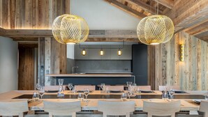 Ein moderner Essbereich mit einem langen Holztisch, mehreren Stühlen mit gemusterten Kissen und zwei großen, kugelförmigen Pendelleuchten.