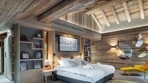Ein modernes Schlafzimmer mit einem großen Bett, Holzbalkendecke, einem Bücherregal und einem einzigartigen Spiegeldesign.