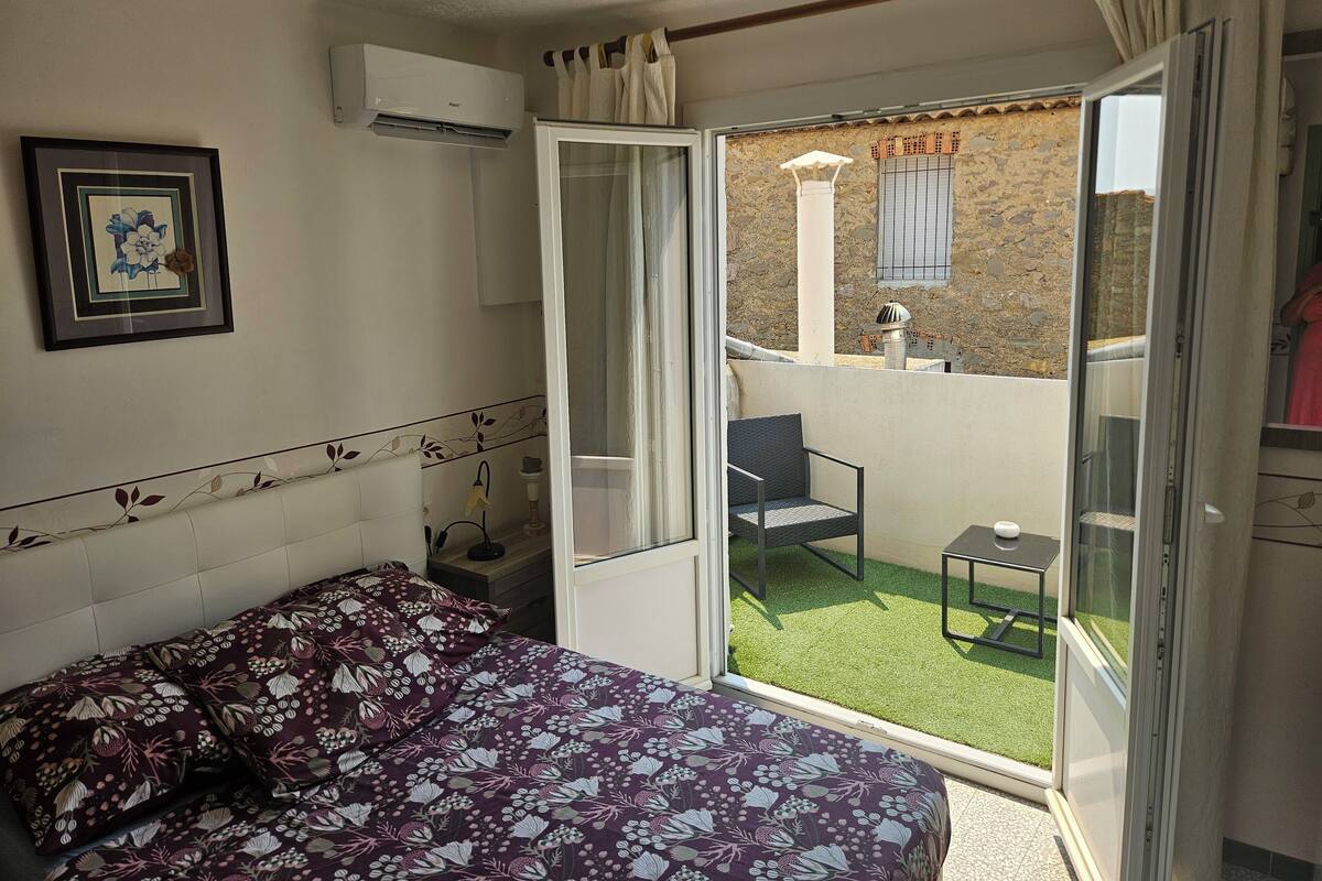 Une chambre à coucher comprenant un lit, une chaise, une petite table et un balcon donnant sur un mur de pierre et une fenêtre.