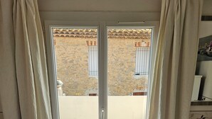 Ein Zimmer mit einem Bett, einem fenster mit Vorhängen und Blick auf ein Gebäude.