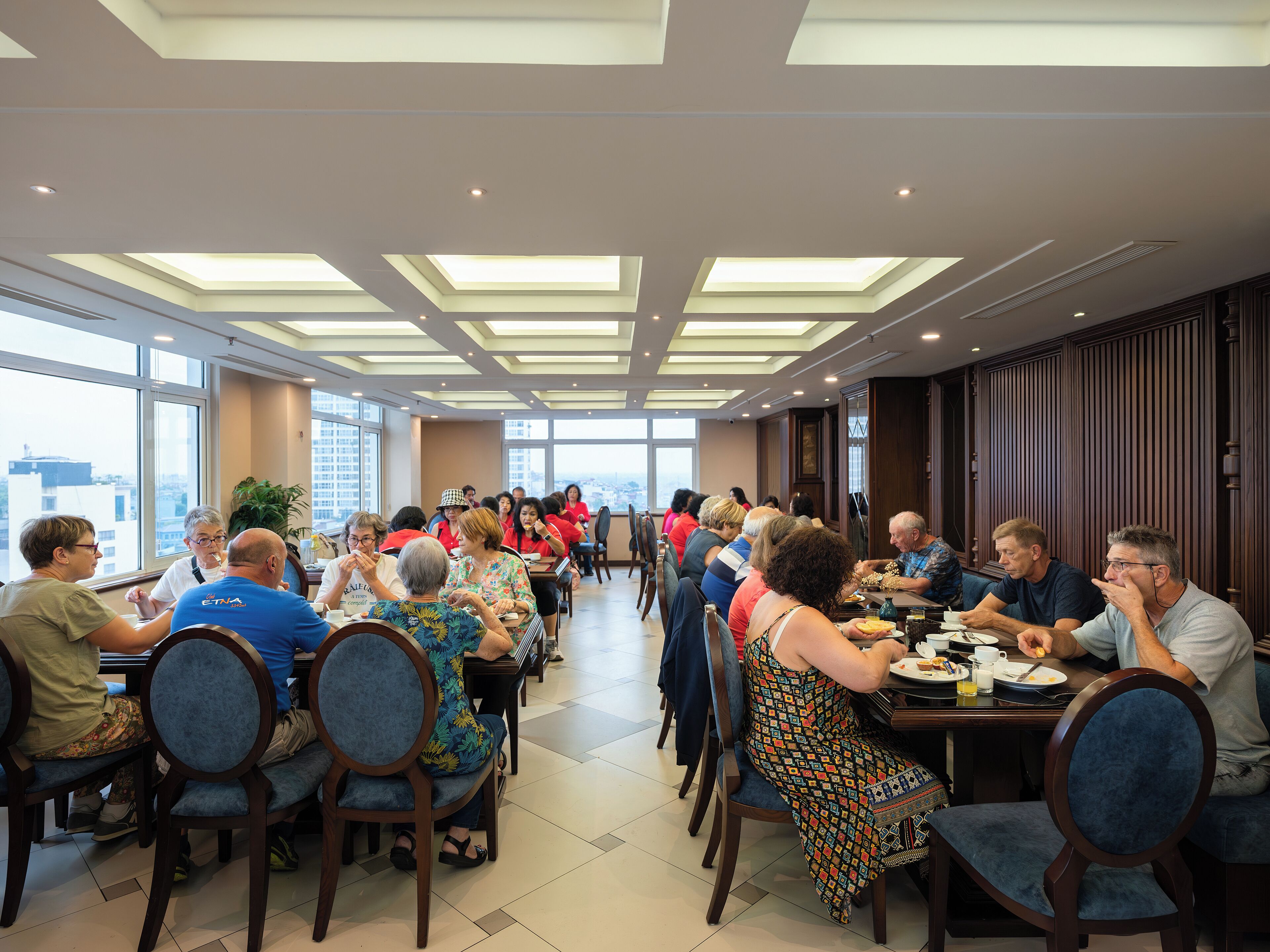 A spacious dining area with high ceilings and skylights, large windows offering a city view, and wooden paneling on the walls.