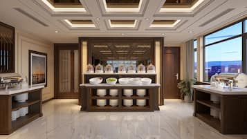 Um hall de hotel moderno com área de buffet central, uma grande janela com vista para a cidade e piso de mármore polido.