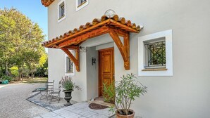 En tvåvåningsbyggnad med en entré som har en träpergola, en trädörr och två fönster med metallgaller.