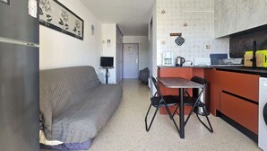 Um espaço de estar compacto com sofá, mesa de jantar com cadeiras, cozinha compacta e uma pequena televisão sobre um suporte.