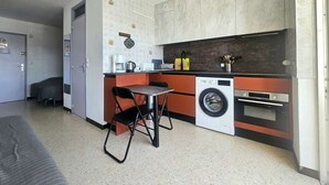 Uma cozinha compacta com máquina de lavar, cafeteira e um pequeno espaço de refeições.