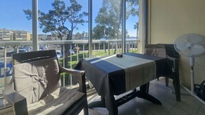 Varanda com mesa, cadeiras, um ventilador e vista para árvores e edifícios.