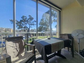 Varanda com mesa, cadeiras, um ventilador e vista para árvores e edifícios.