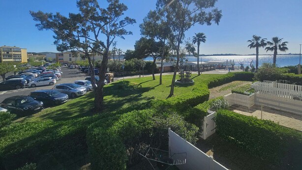 Um estacionamento com carros, uma área gramada com árvores e vista para o mar.