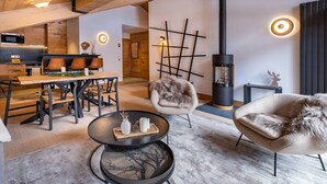Un intérieur moderne avec un plafond en bois, un coin repas avec une table et des chaises en bois, un coin salon confortable avec un fauteuil en fourrure et un poêle noir.
