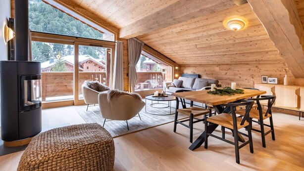 Une pièce chaleureuse de style loft, avec un plafond en bois, une grande fenêtre, une cheminée, une table à manger et des sièges confortables.