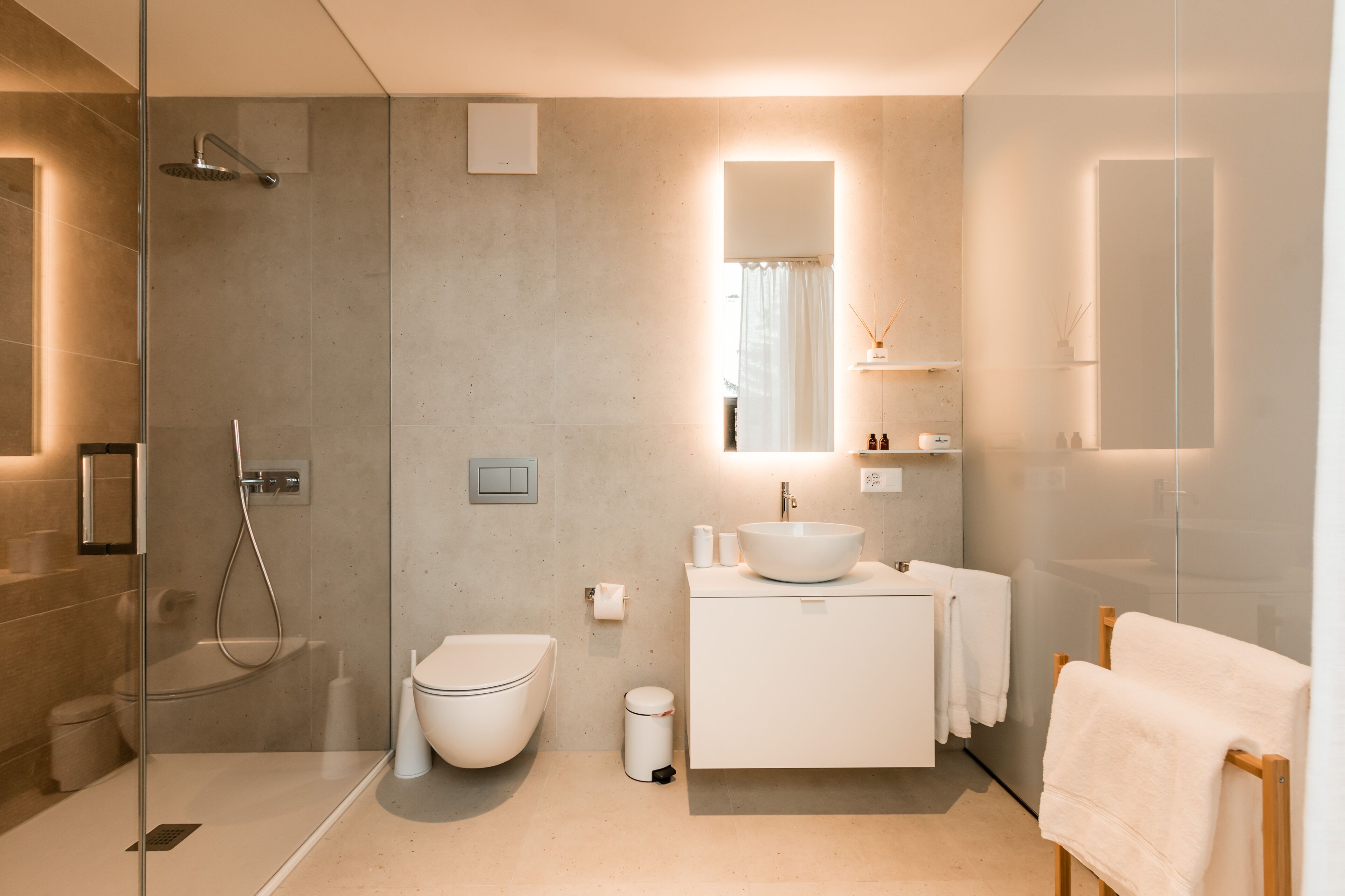 A modern bathroom with a glass-enclosed shower, a white toilet, a sink with a mirror above, and a towel rack.