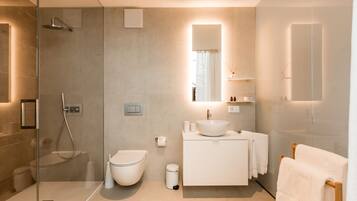 A modern bathroom with a glass-enclosed shower, a white toilet, a sink with a mirror above, and a towel rack.