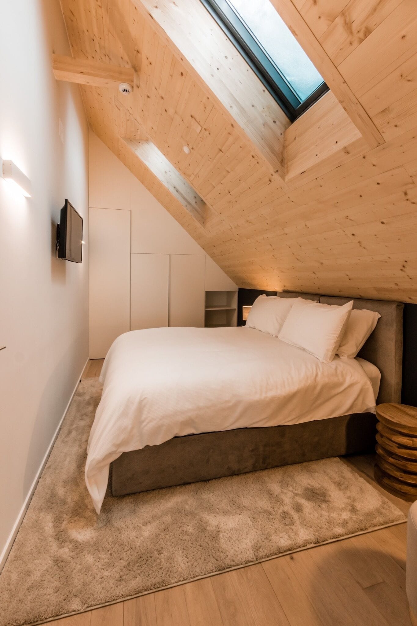 A bedroom with a sloped ceiling, a bed, a TV, and a window.