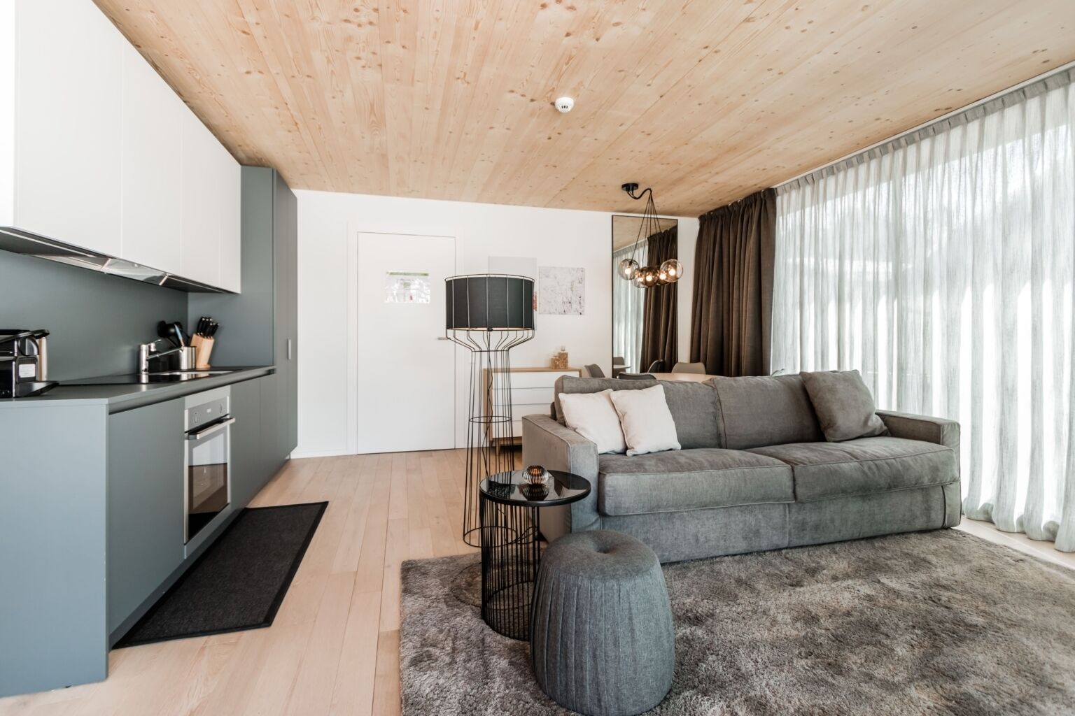 Un espacio habitable moderno con cocina, sofá gris y una mesa redonda.