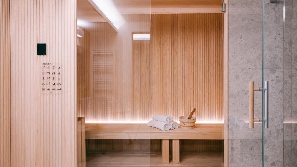 Una sauna de madera con un banco, toallas y un cubo de madera.