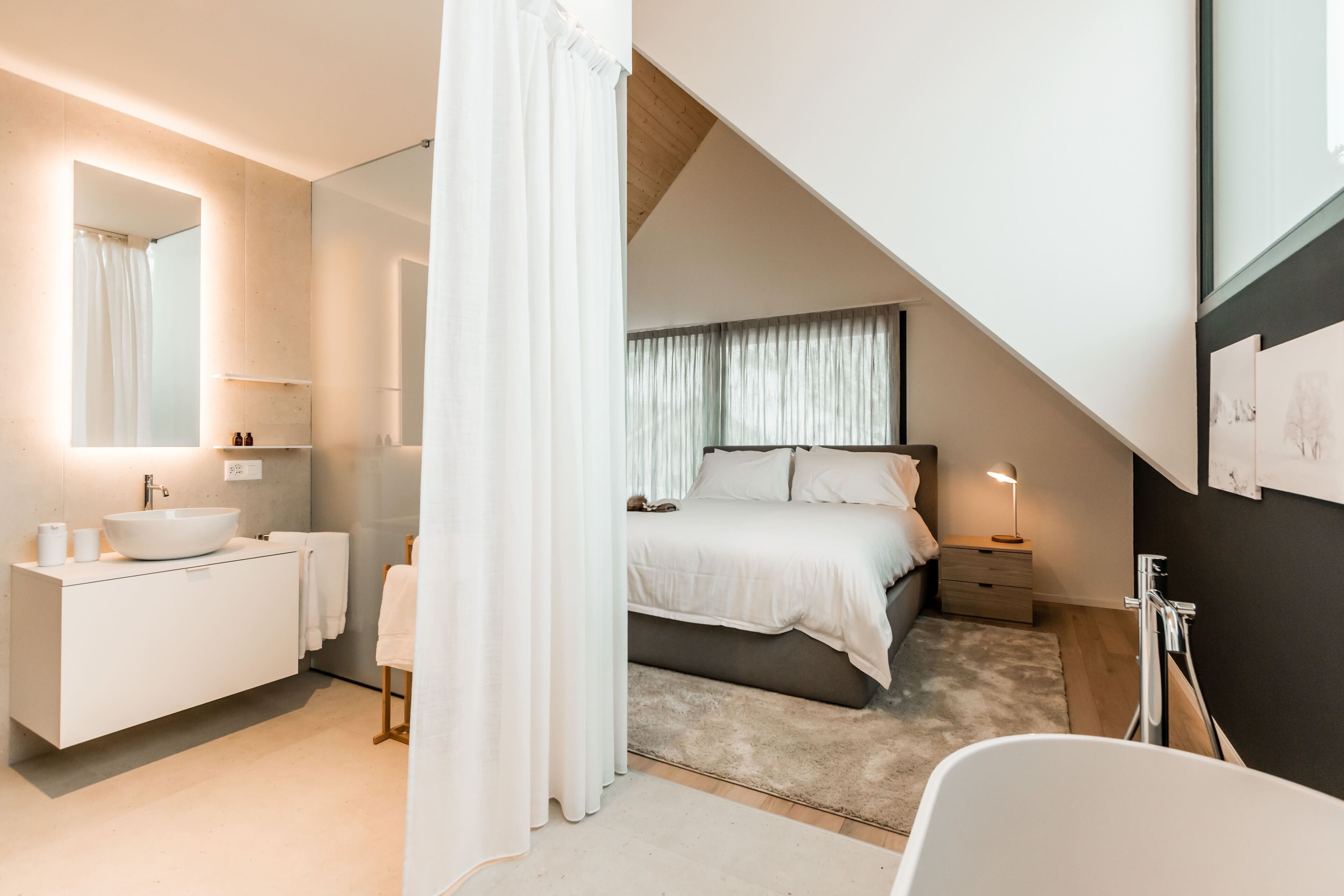 Une chambre à coucher moderne avec un grand lit, une table de chevet, une commode, une salle de bain avec un lavabo et un miroir.