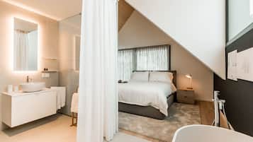 Une chambre à coucher moderne avec un grand lit, une table de chevet, une commode, une salle de bain avec un lavabo et un miroir.